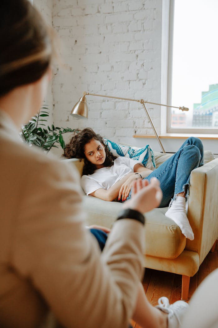 A therapist converses with a young adult on a sofa, focusing on mental health.