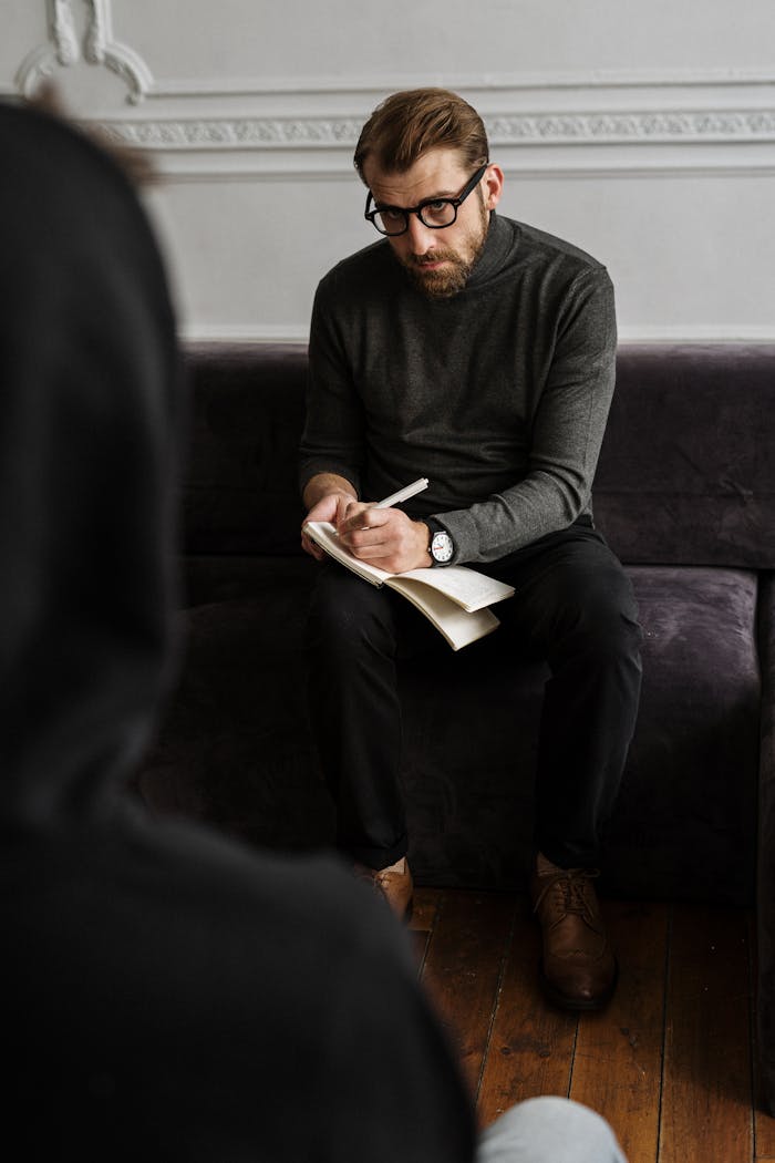 Bearded therapist taking notes during a private counseling session indoors.