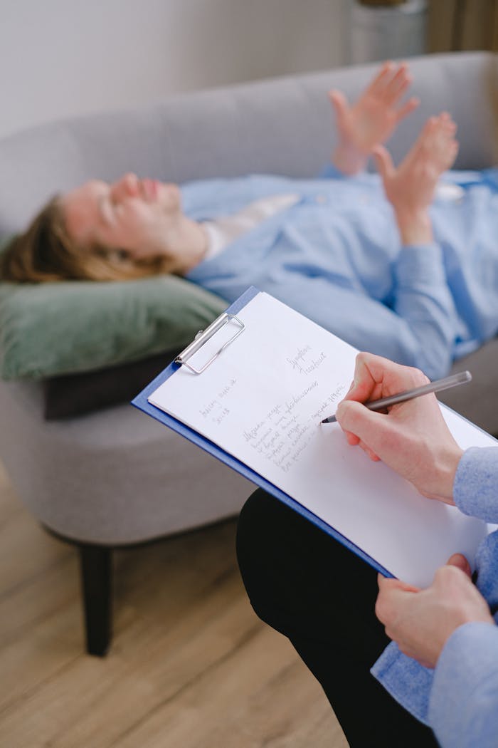 Therapist taking notes while a patient lies on the couch during a therapy session.