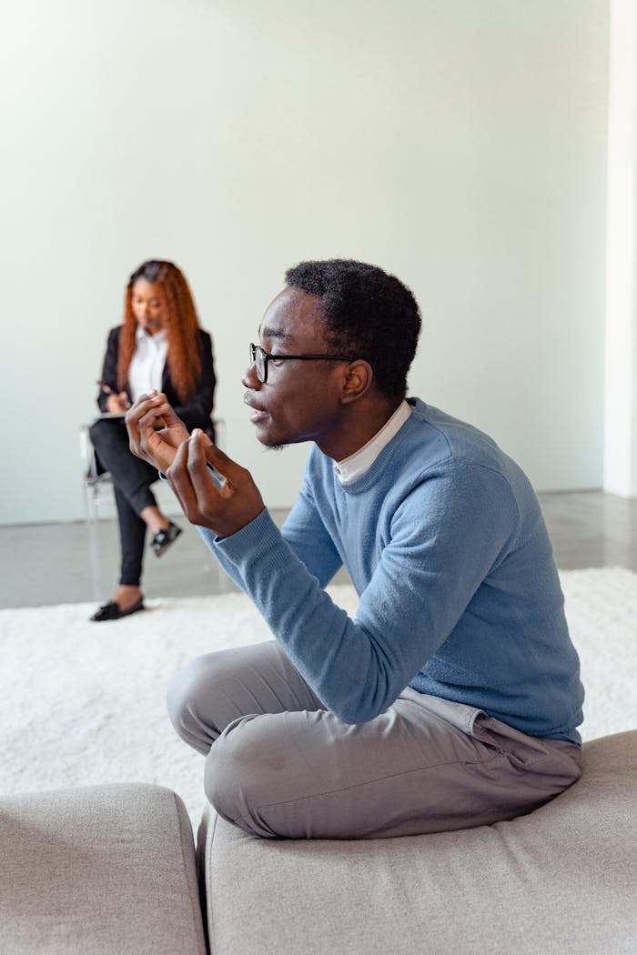 An African American man expresses himself during a therapy session indoors, highlighting mental health discussions.