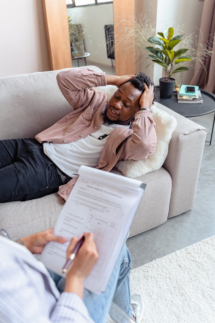 A therapist sessions with a worried man lying on a sofa, addressing mental health concerns.